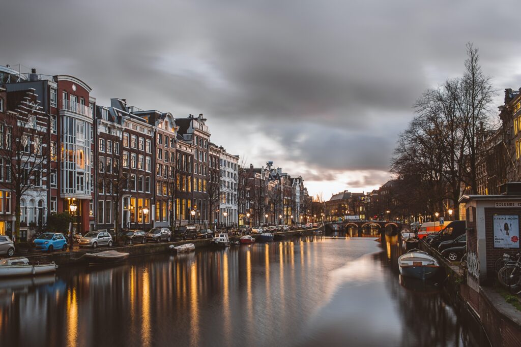 Klassischer Kanal in Amsterdam, bei Abendbeleuchtung sind links und rechts Häuser zu sehen und in der Mitte das stille Wasser
