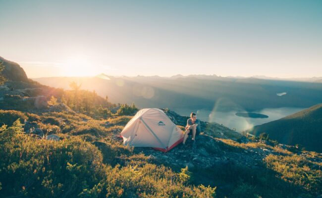 Mensch sitzt vor seinem Zelt auf einem Berg mit toller Aussicht