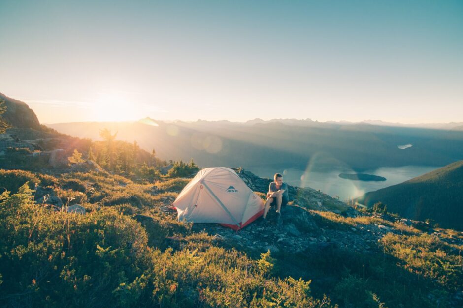 Mensch sitzt vor seinem Zelt auf einem Berg mit toller Aussicht