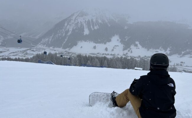 Ich sitze mit meinem snowboard oben auf dem Berg in Livigno bei schlechten Bedingungen