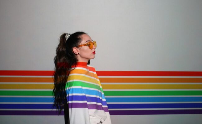 Frau vor einer in LGBTQIA* Farben bemalte Wand