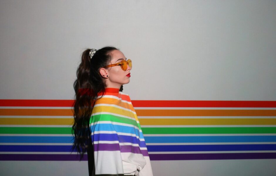 Frau vor einer in LGBTQIA* Farben bemalte Wand