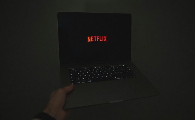 Laptop mit Netflix drauf im dunkeln von einer Hand gehalten